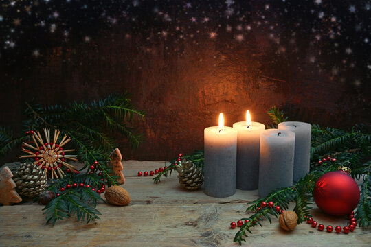 Second Advent, two of four candles are lighted, red bauble, straw star, fir branches and Christmas decoration on rustic wooden planks against a dark brown background, copy space