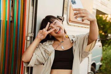 Asian young woman gesturing and taking selfie on cellphone by trailer
