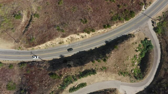 Overhead aerial new sport cars driving zigzag by empty mountain highway road in Malibu canyon mountain. Top down shot of exotic performance cars racing down road on sunny summer day, California USA 4K