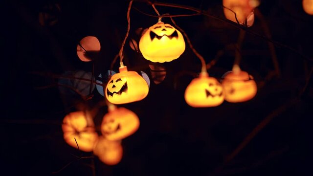 Close-up of a garland jack lantern pumpkins glow in the dark on a tree in the city