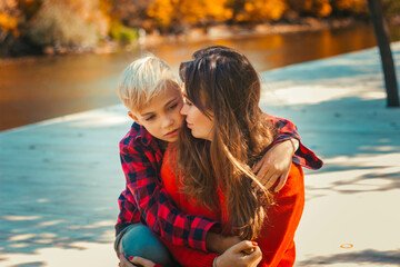Fototapeta na wymiar Boy son hugs his mother in red sweaters in the fall at the pond 