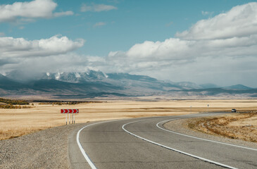 Empty mountain road with a single car and traffic sign. Blue sky, yellow grass.