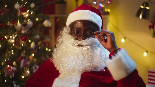 Happy Santa Claus wearing glasses portrait. Smiling african american man in christmas costume of santa close-up, looking in camera. Cheerful st Nicholas posing in living room. New year time concept.