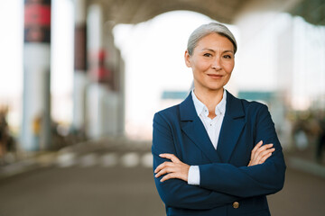 Grey asian woman in jacket smiling while posing on airport parking