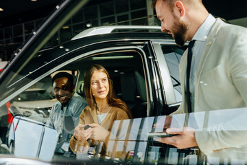 Diverse couple sitting in auto while talking with salesman