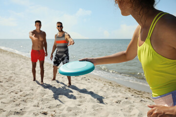 Obraz premium Friends playing with flying disk at beach on sunny day