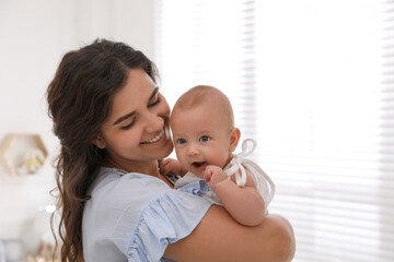 Happy young mother with her cute baby near window at home