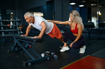 Old man, push-up exercise on bench, female trainer