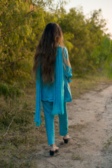 Girl in Pakistani dress walking on a path surrounded by greenery 