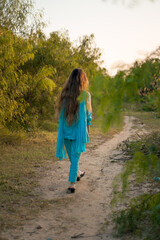 Girl in Pakistani dress walking on a path surrounded by greenery 
