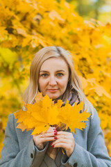 A woman holds maple yellow leaves in her hands in a park against a background of trees