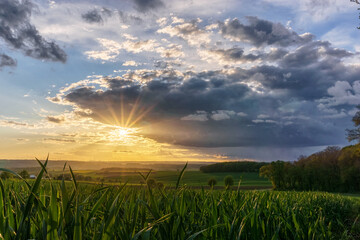 sunset with dramatic sky over rural landscape with agricultural green fields, Eifel, Germany