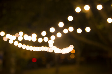 Blurred abstract background, backyard illumination, light in the evening garden, electric Defocused garland. Lamp garland of light bulbs on trees illuminate night scene