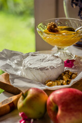 Brie cheese or camembert on cheese platter with walnuts, honey in a bowl, apples next to it . Closeup view, selective focus