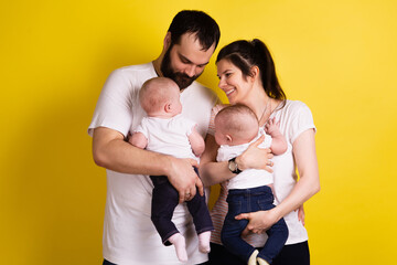 a man and a woman stand with their backs to each other and hold twin children in their arms. man and woman are happy and wearing white t-shirts