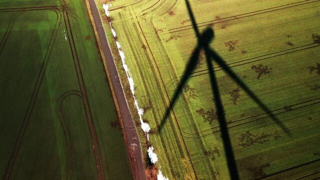 Aerial view of a field with the rotating shadow of a wind turbine