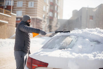 A young man cleans his car after a snowfall on a sunny, frosty day.