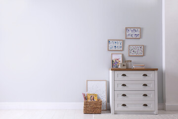 Wooden chest of drawers with books and decor near white wall in room, space for text. Interior design