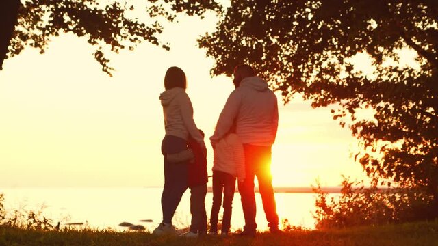 Loving family walks in the countryside during sunset. Mom and Dad hug and play with their son and daughter. The concept of love, parental care and children.