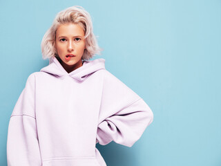 Young beautiful upset female in trendy summer hoodie. Sexy carefree woman posing near blue wall in...