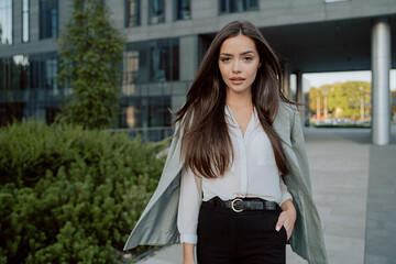 Attractive girl with brown hair walks out of corporate building for break, dressed in smart shirt and jacket imposed on back, walks outside past glass skyscraper, secretary, businesswoman, boss