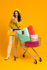 White excited woman posing with cellphone and shopping cart