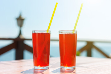 Two glasses with berry juice and strawberries on the table of a street cafe against the background of the sea.