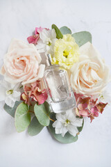 Obraz na płótnie Canvas Square bottle of perfume with white roses, pink hydrangea, eucalyptus branch, water drops on the white background. Summer, spring flower smell. Perfume inside different flowers wreath. Girlish smell.