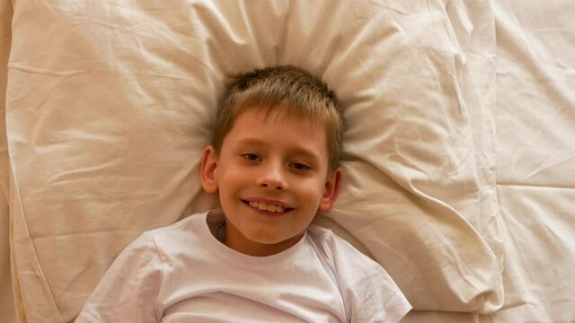 The child wakes up in the morning theme. Positive Caucasian boy 7-9 lying on the bed stretching his arms after sleep and smiling. A carefree person starts a new day. Schoolboy going to school