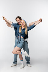 excited couple in stylish denim clothing holding hands while posing on white