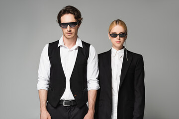 front view of young couple in dark sunglasses and black and white clothing isolated on grey
