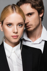 blonde woman and brunette man in black and white clothes looking at camera isolated on grey