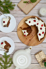 A Christmas cake and two pieces on the wooden background with teapot, gift and branches of the Christmas tree. Horizontal frame.