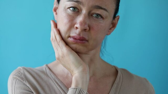 Teeth Problem. Gumboil, flux, bruise and swelling of cheek. Woman holds hand to cheek. She removes hand from the sore spot. Two cheeks swollen. Inflammation after implant placement, swelling and pain