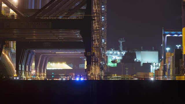 Felixstowe, United Kingdom - October 24 2021: A night timelapse of freight being lifted from port vehicles to be loaded onto a ship, which can be seen at the edge of the frame.