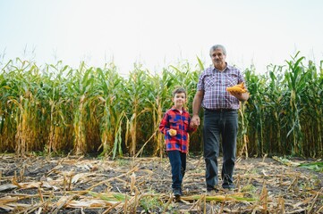 Grandfather and grandson with ripe corn ears taking selfie near dry plants while working in agricultural field together