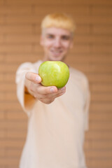 Healthy eating, organic food, fruits and people concept - Close-up of a green apple held in the hand of a smiling Caucasian man showing it to the camera on a brick wall background