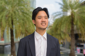 Portrait of happy Asian businessman thinking outdoors in the city