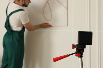 Cross line laser level and handyman hanging picture on white wall