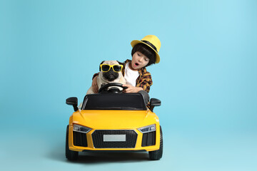 Little boy with his dog in toy car on light blue background