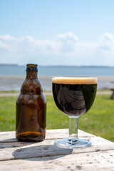 Glass of dark strong belgian beer served on outdoor terrace with green grass meadow on background