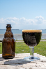Glass of dark strong belgian beer served on outdoor terrace with green grass meadow on background