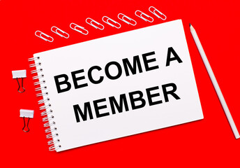 On a bright red background, a white pencil, white paper clips, and a white notebook with the text BECOME A MEMBER