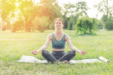 A middle-aged woman practices yoga outdoors. Woman meditating in the park in lotus position