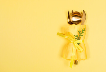 Xmas table setting with gold cutlery set in napkin with arborvitae branch on yellow. Copy space.