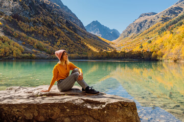 Woman posing at crystal lake in autumnal mountains. Mountain lake and traveller waman