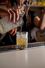 Bartender is preparing a cocktail at the bar. The hand of the bartender is pouring a ready-made cocktail into a glass