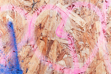 Particleboard chipboard texture with pink and blue spray paint heart, waste-wood product, wood chips, sawmill shavings, sawdust