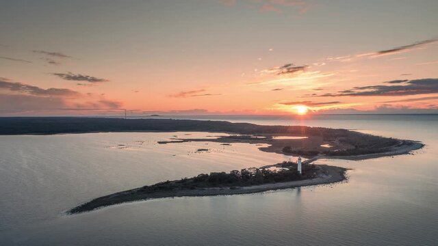 Time lapse of Swedish lighthouse Lange Erik on island in north of Oeland during sunset from above, flat ocean, moving clouds and sun sinking down the horizon
