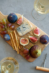 Two wineglasses of vintage chardonnay with delicious appetizers. Couple of glasses of white wine, italian breadsticks, whole and cut figs and grapes. Interior background. Close up, copy space.